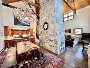 A spacious interior with a stone fireplace, a dining area with a large table and chairs, a kitchen with wooden cabinets, and a staircase leading to an upper level. - Secluded Cottage with Stunning Sights in Winhall, Vermont (Winhall)