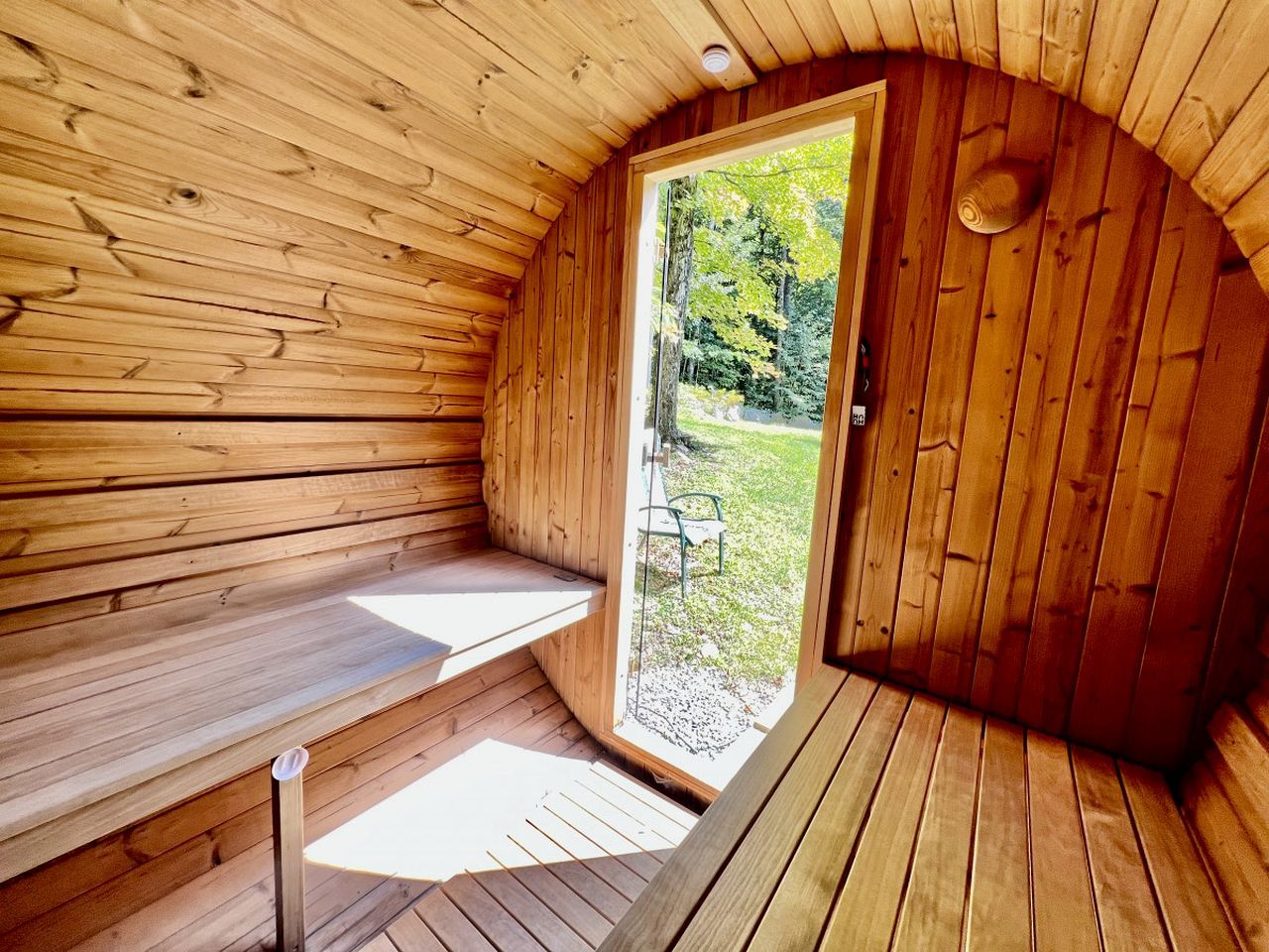 Un sauna en bois avec un banc, une porte donnant sur l’extérieur et une vue sur la verdure.