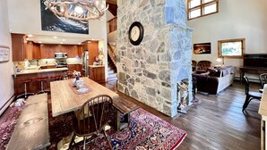 A spacious interior with a stone fireplace, a dining area with a large table and chairs, a kitchen with wooden cabinets, and a staircase leading to an upper level. - Secluded Cottage with Stunning Sights in Winhall, Vermont (Winhall)