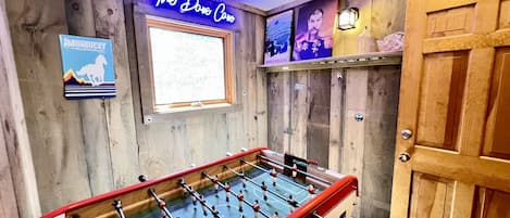 Una habitación con mesa de fútbol de mesa, paredes de madera, letrero de neón y una bola de discoteca.