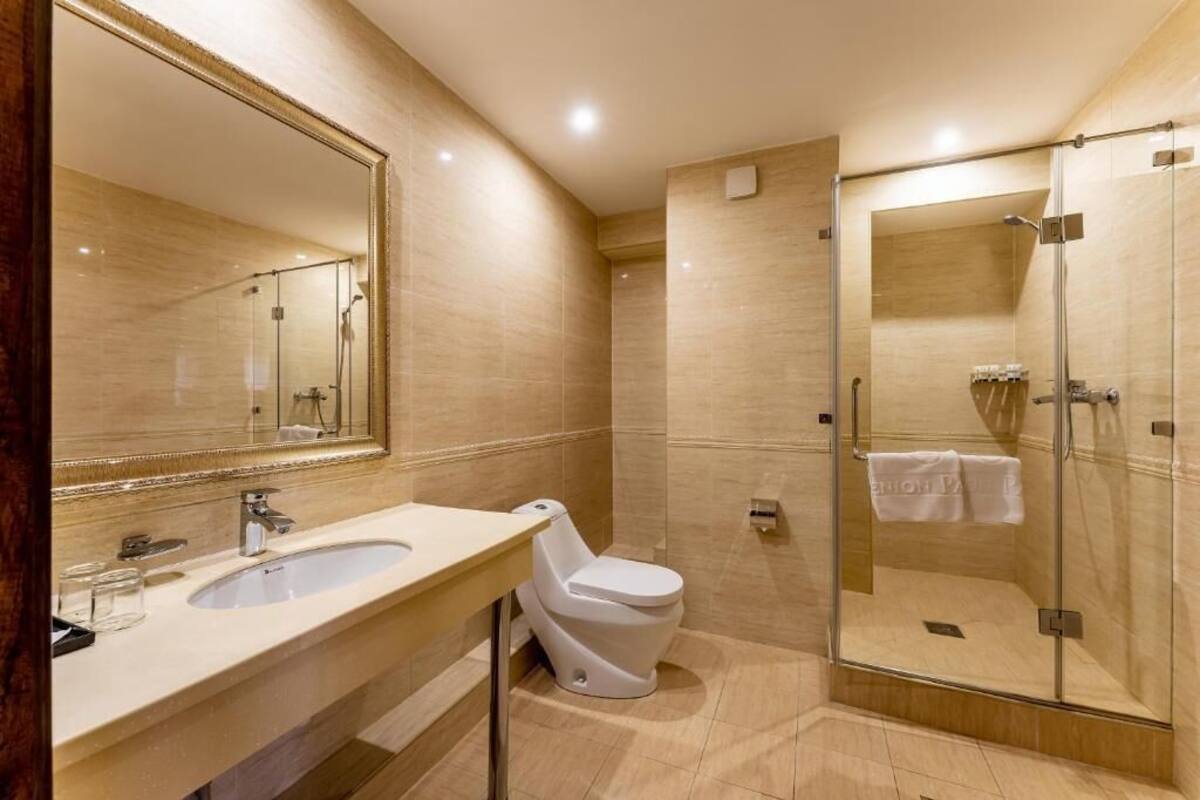 A modern bathroom with a large mirror, a sink, a toilet, and a glass-enclosed shower area.