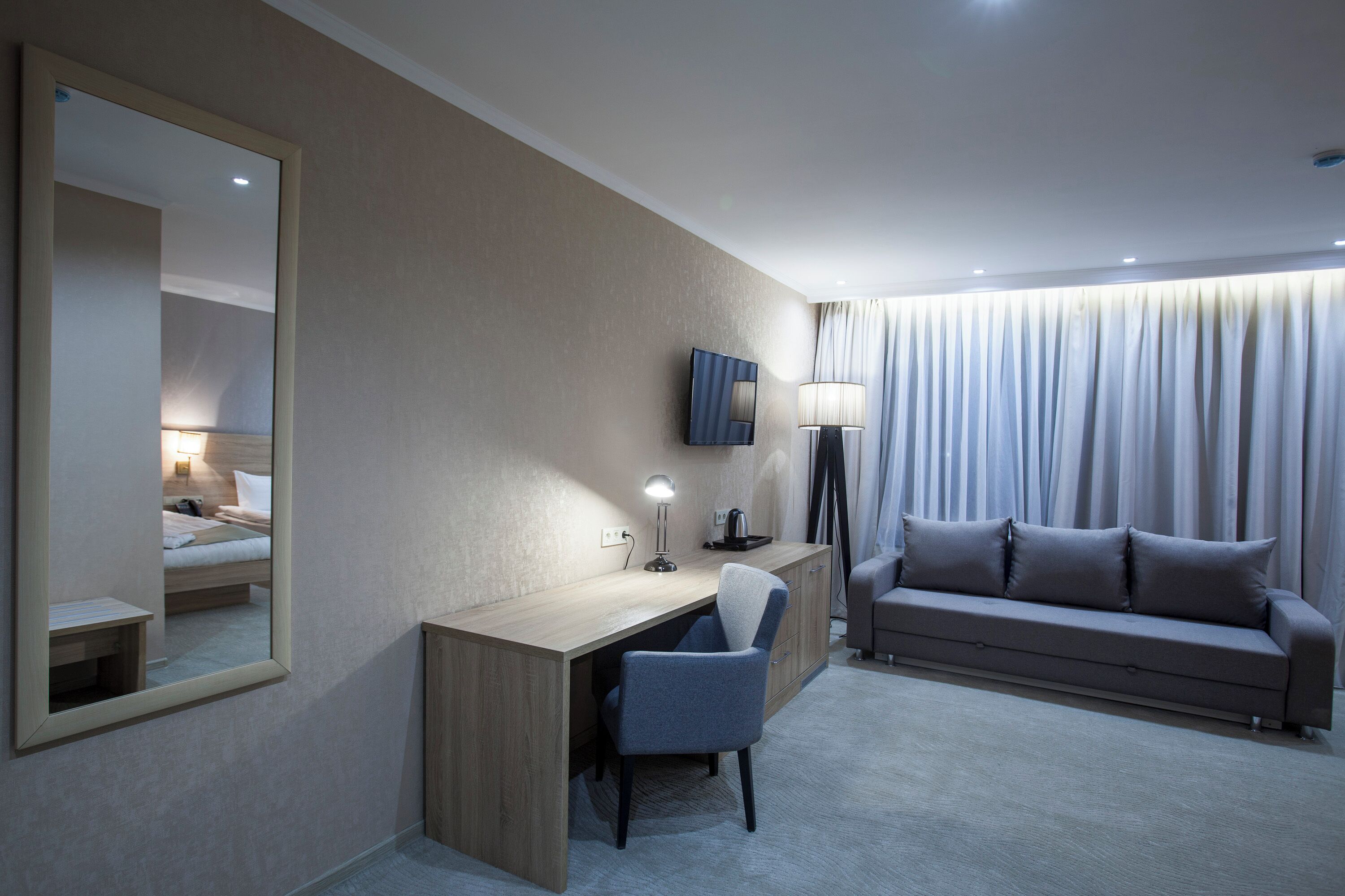 A hotel room with a desk, chair, sofa, and a large mirror.