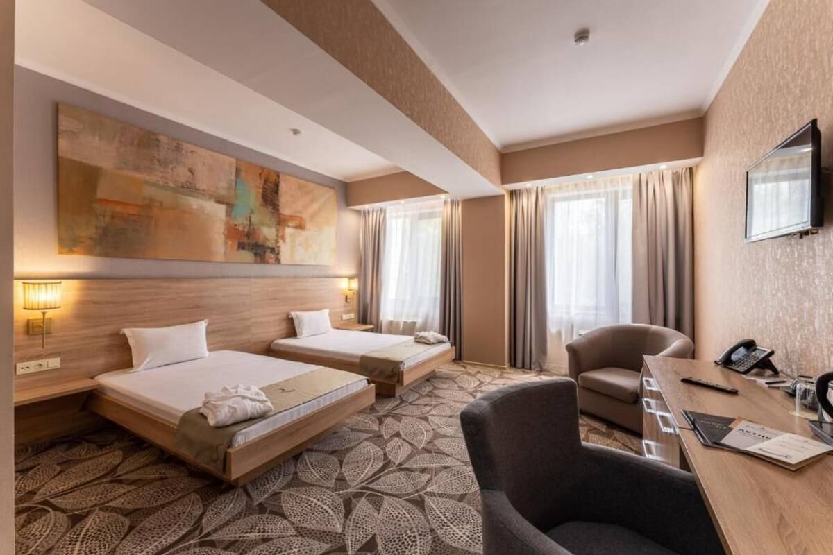 A hotel room with two beds, a desk, a chair, a television, and a large abstract painting on the wall.