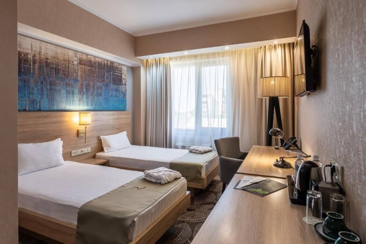 A hotel room with two beds, a desk, a lamp, and a TV.