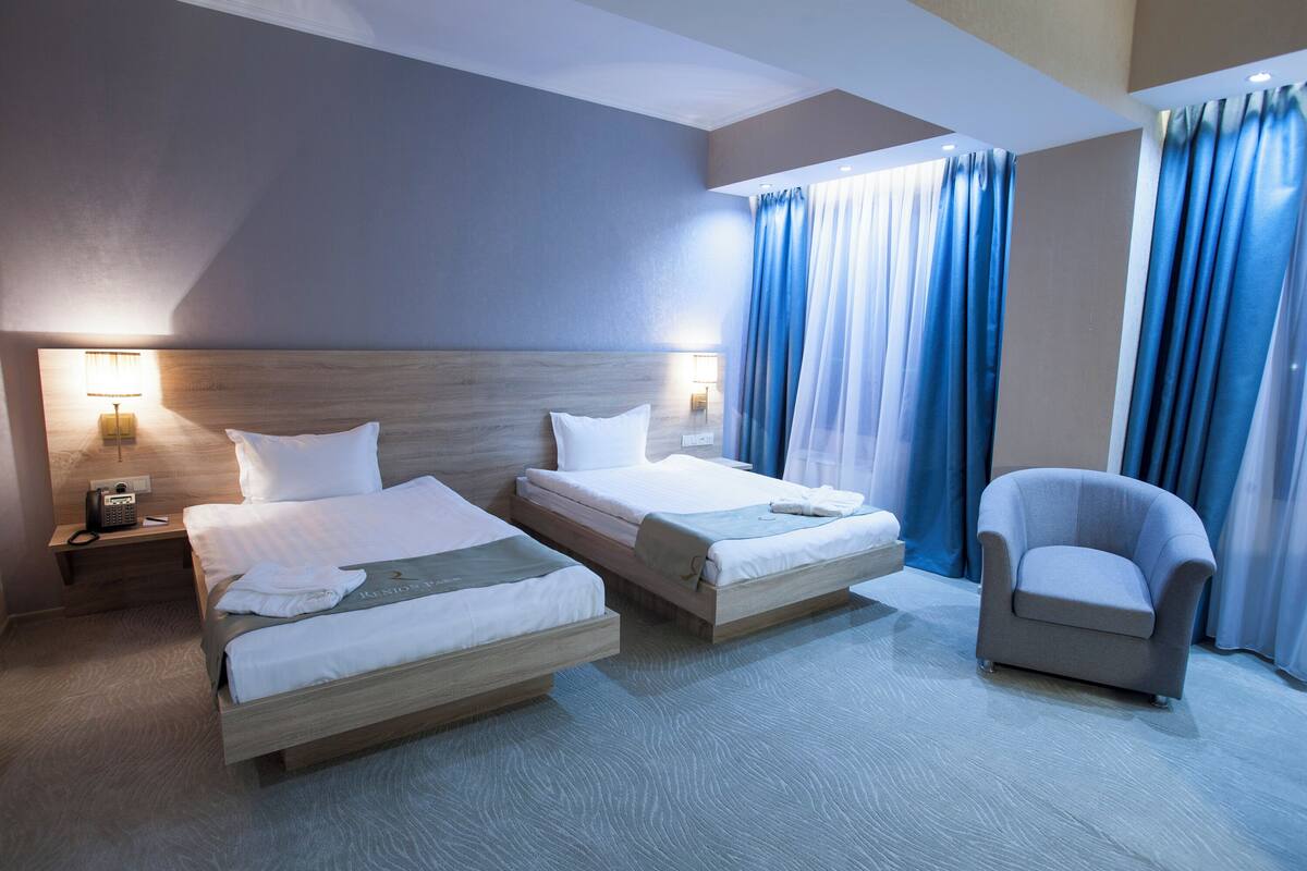 A hotel room with two beds, a chair, and a nightstand with a lamp.