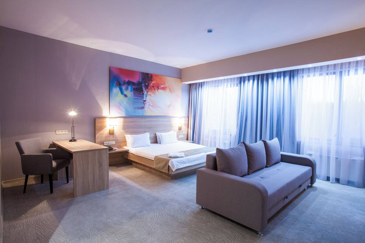 A hotel room with a bed, a sofa, a desk, and a chair.