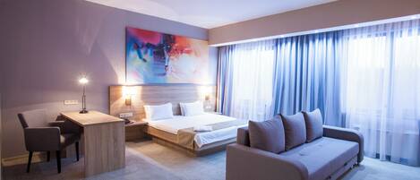 A hotel room with a bed, a sofa, a desk, and a chair.