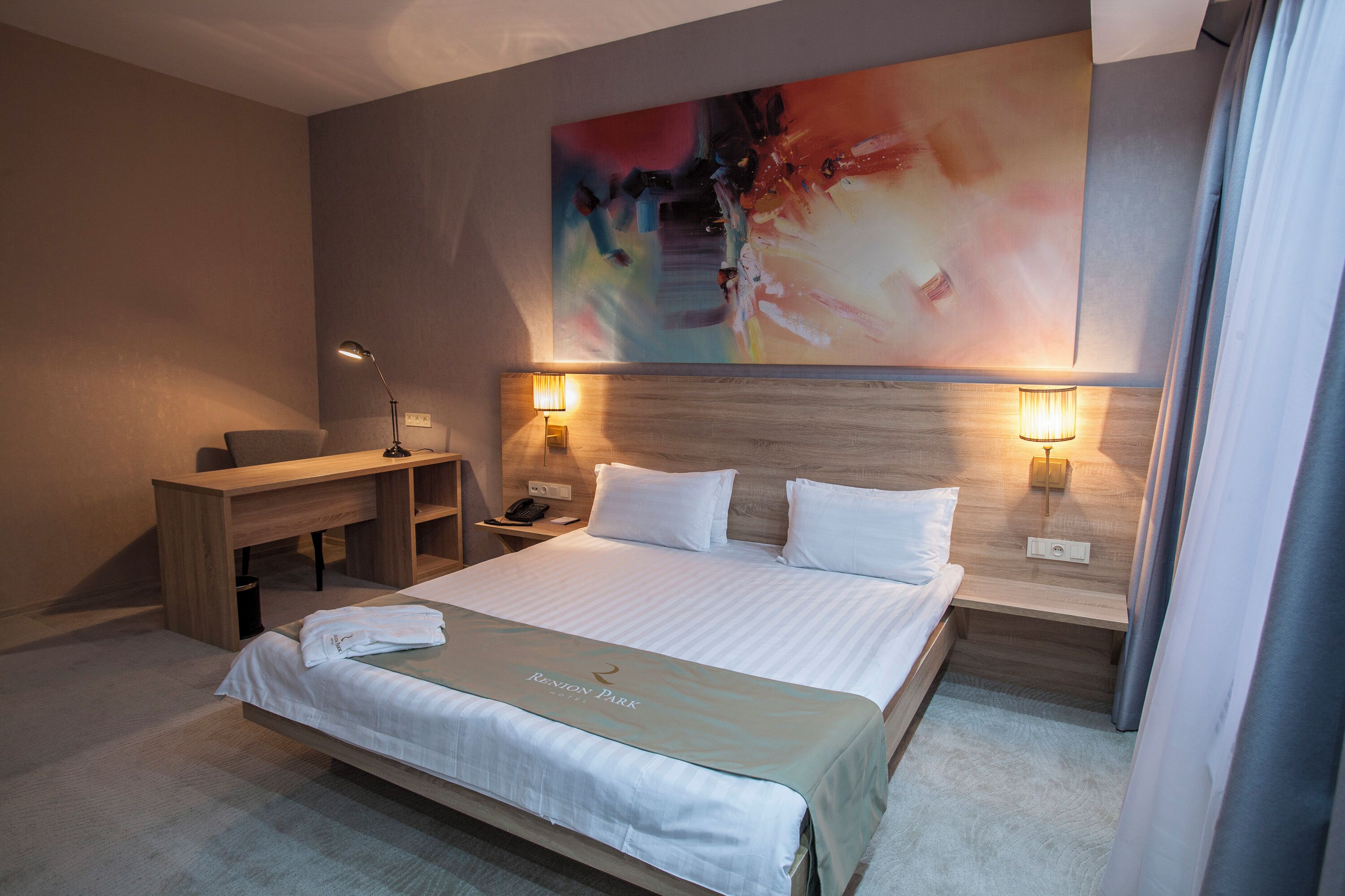A hotel room with a bed, desk, and two bedside lamps.