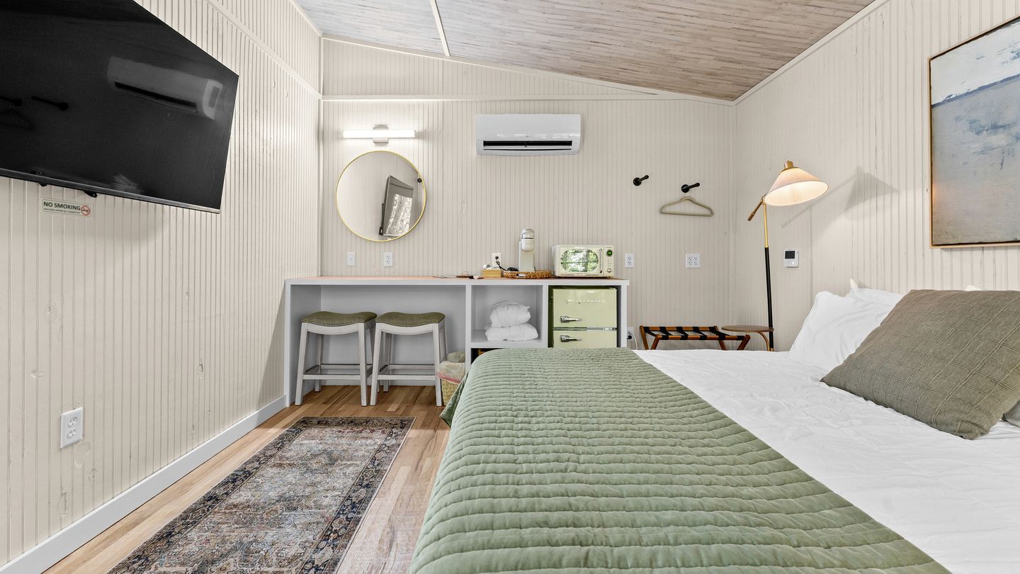 Ein Hotelzimmer mit einem Bett, einem Schreibtisch mit zwei Stühlen, einem Spiegel, einer Lampe und einem Fernseher.