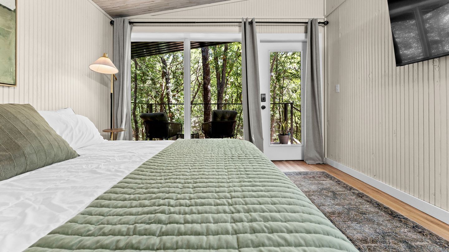 Ein Schlafzimmer mit einem Bett, einem Fenster und Blick auf Bäume.