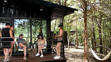 Un espace extérieur moderne, aménagé avec des sièges et protégé par une paroi de verre, entouré d’arbres et agrémenté d’un hamac.