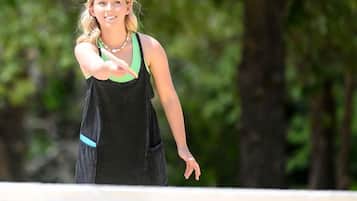 A person standing on a tennis court with a net in the foreground.