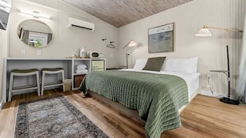 A bedroom with a bed, bedside tables, a desk with a chair, a lamp, a mirror, and a wall-mounted air conditioner.