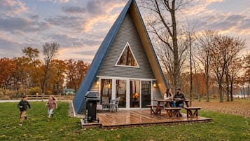 A triangular house with a deck, a grill, and a table with chairs.