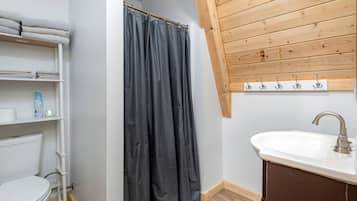 A bathroom with a toilet, a sink, a shower curtain, and a shelf with towels.