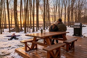 Une table de pique-nique en bois, placée dans un décor extérieur enneigé, avec un barbecue et des bancs.