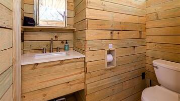 A wooden cabin-style bathroom with a sink, toilet, and a window.