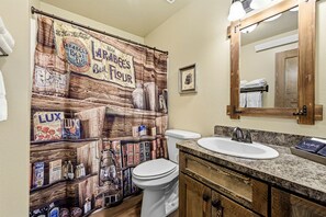 Een badkamer met een douchegordijn in vintage-stijl, een wit toilet, een wastafel met een granieten aanrechtblad en een houten opbergmeubel.