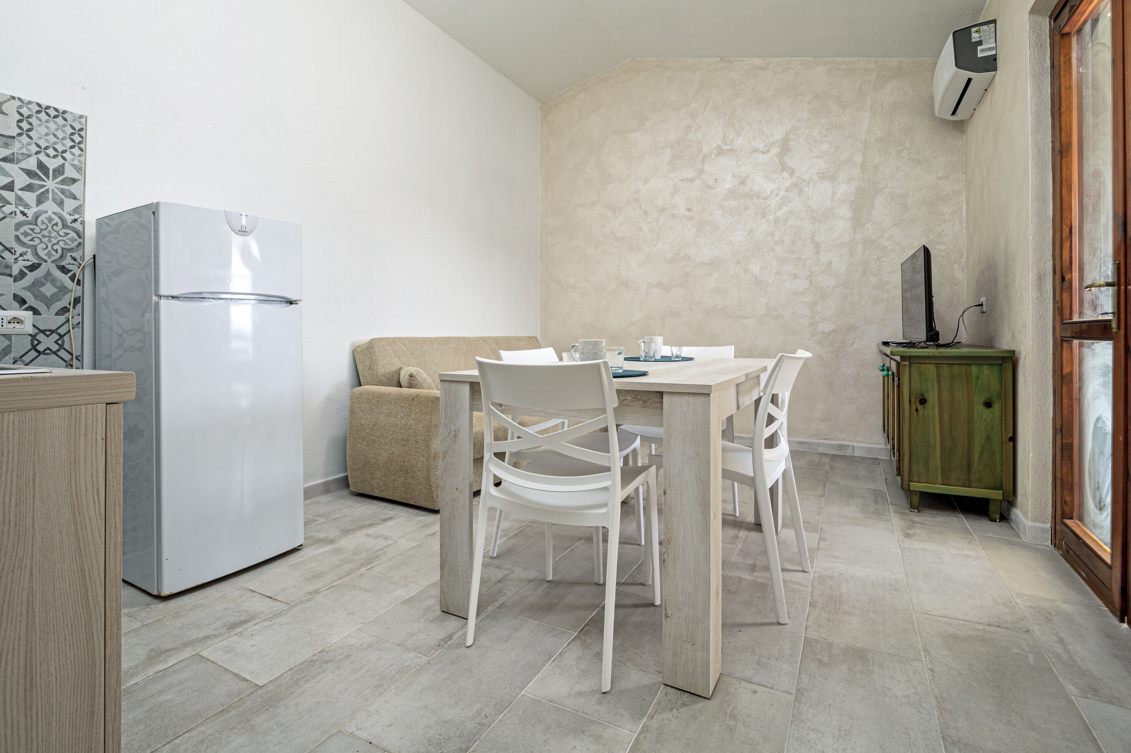 A compact kitchen with a refrigerator, dining table, chairs, and a cabinet.