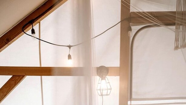 Una camera da letto con un letto, un piccolo comodino, una lampada a sospensione e una finestra con tende trasparenti.