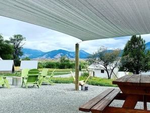 A covered outdoor seating area with a view of mountains, a picnic table, and green chairs.