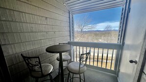 A covered outdoor seating area with a table and chairs, a door, and a view of a landscape with trees and mountains. - Mountain Cabin Great for a Family Retreat in Vermont (Stratton)