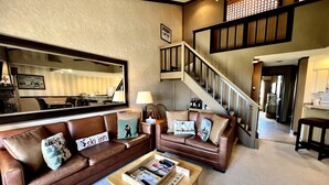 A living room with a brown leather sofa, a wooden coffee table, and a staircase leading to an upper level. - Mountain Cabin Great for a Family Retreat in Vermont (Stratton)