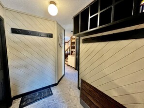 Un couloir avec un plancher en bois, une horloge et une porte donnant sur un espace cuisine.