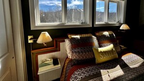 A bedroom with a bed, two bedside lamps, a window with a view, and a bedside table with a lamp. - Mountain Cabin Great for a Family Retreat in Vermont (Stratton)