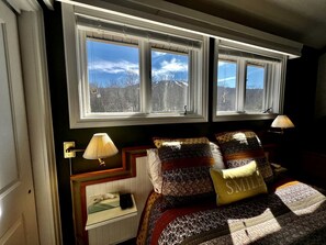 Ein Schlafzimmer mit einem Bett, zwei Nachttischlampen, einem Fenster mit Blick und einem Nachttisch mit Lampe.