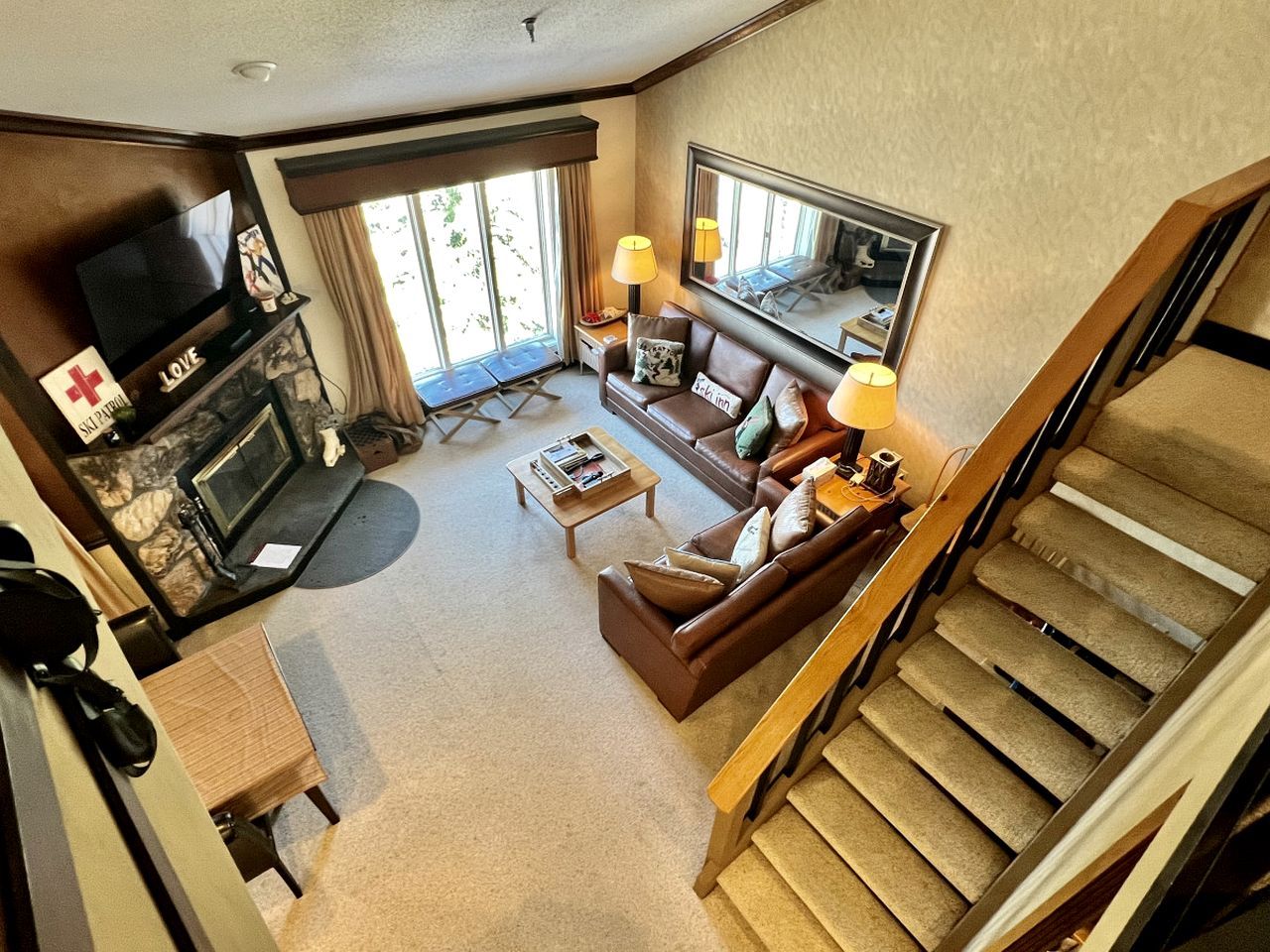 A hotel living room with a fireplace, a sofa, a coffee table, a TV, and a staircase.