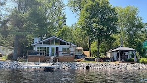 A lakeside cabin with a dock, a covered outdoor seating area, and a wooden deck.