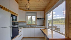 A modern kitchen with white cabinets, a built-in microwave, and a large window overlooking a lake.