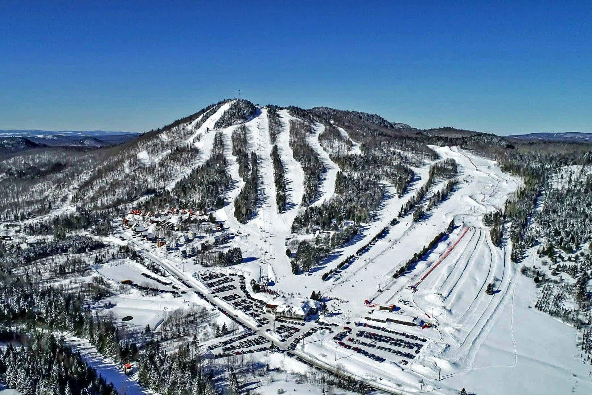 A snow-covered ski resort with multiple ski trails and a parking area.