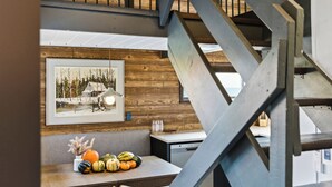 A dining area with a wooden wall, a framed picture, and a table with pumpkins. - Mont Orignal | Private Hot Tub | Alpenglow (Lac-Etchemin)