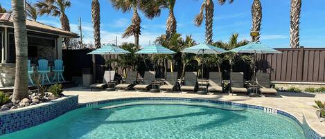 A swimming pool with lounge chairs and umbrellas, surrounded by palm trees.
