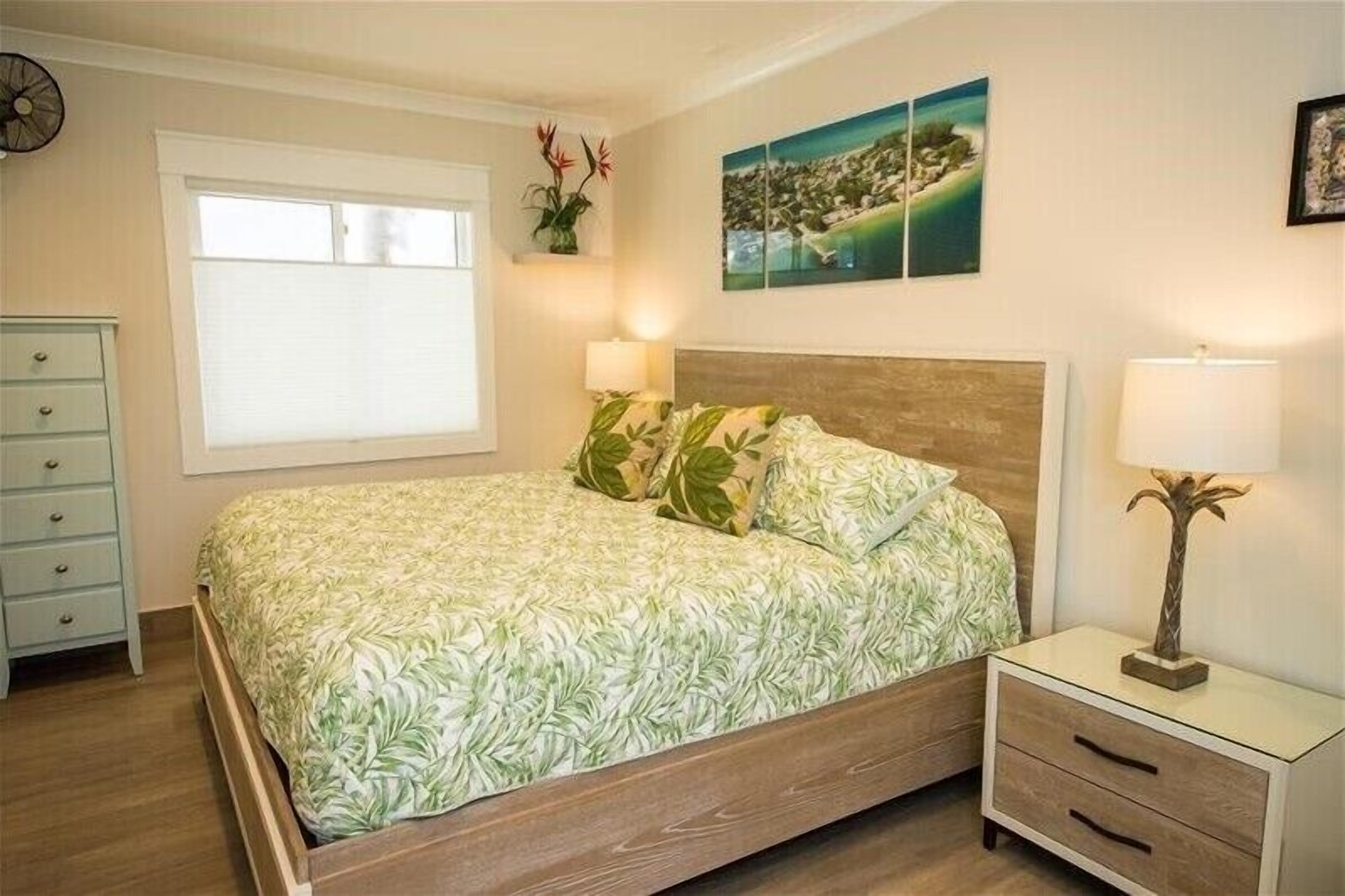 A bedroom with a bed, a nightstand, a dresser, a window, and wall art.