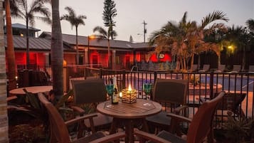 Ein Patio mit runden Tischen und Stühlen, ein Schwimmbecken und ein Gebäude im Hintergrund mit roter Beleuchtung.