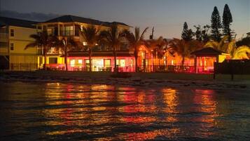Ein Strandhotel mit mehreren Gebäuden, Palmen und einer spiegelnden Wasseroberfläche.