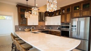 A modern kitchen with a large island, dark wooden cabinets, stainless steel appliances, and a unique chandelier. - The Rod and Reel Resort-Grand Suite 8 (Anna Maria)