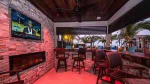 A bar area with stone walls, a flat-screen TV, and outdoor seating with a view of palm trees. - The Rod and Reel Resort-Grand Suite 8 (Anna Maria)