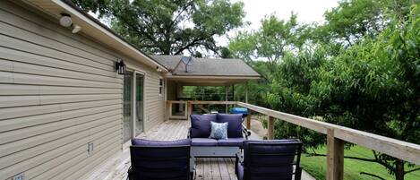 A covered outdoor deck with a sofa and chairs, a barbecue grill, and a wooden railing.