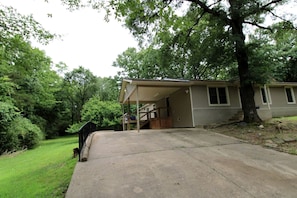 A single-story house with a covered garage, a front yard, and a large tree. - Charming Cottage Nestled Amidst Trees in Hot Springs, Arkansas (Hot Springs)