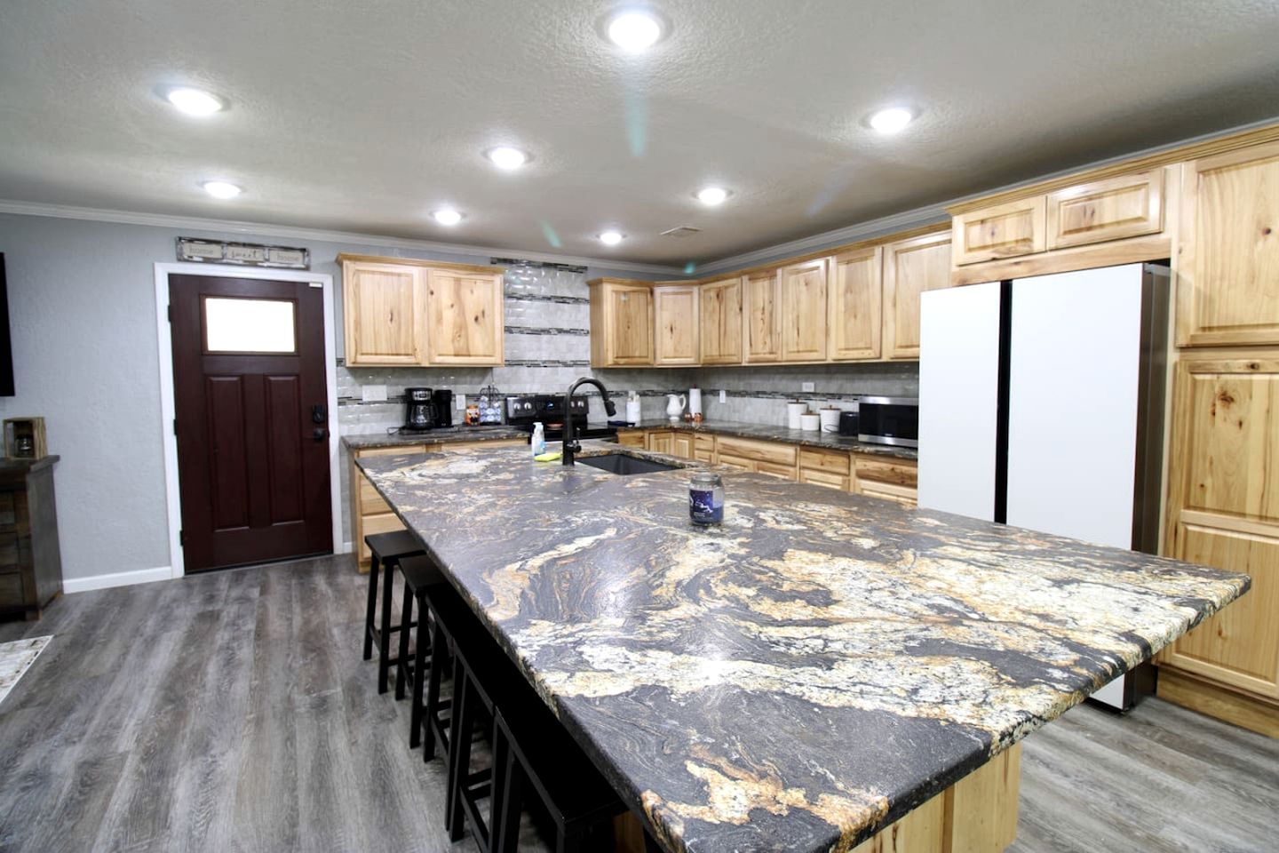 Una cocina con armarios de madera, encimera de granito y refrigerador de acero inoxidable.