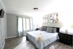 A bedroom with a bed, nightstands, a dresser, a window with curtains, and artwork on the wall. - Charming Cottage Nestled Amidst Trees in Hot Springs, Arkansas (Hot Springs)