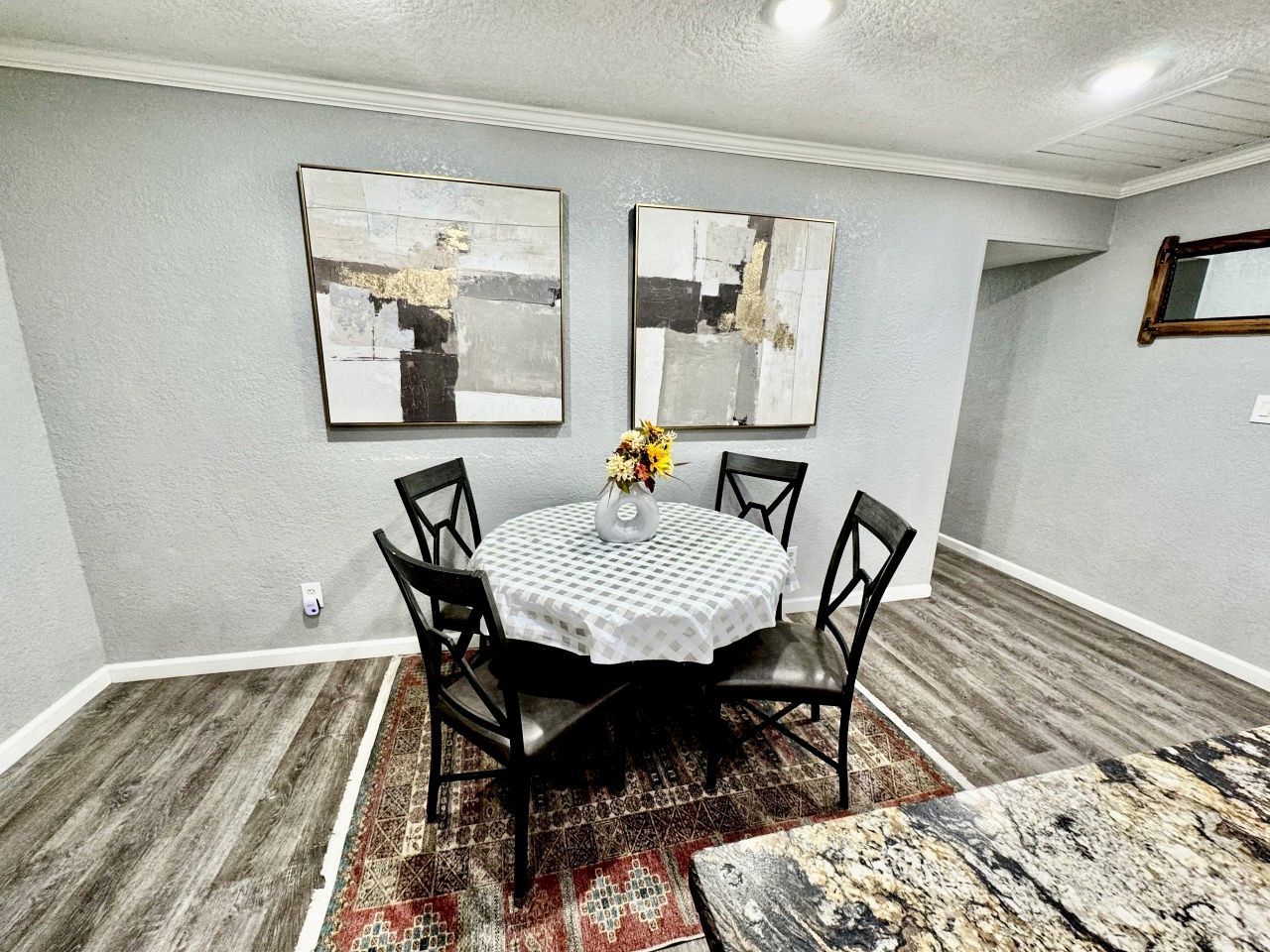 A dining area with a round table, black chairs, a white tablecloth, and two abstract paintings on the wall.