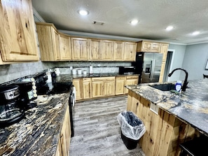 A kitchen with wooden cabinets, a black countertop, a stainless steel refrigerator, and a sink. - Charming Cottage Nestled Amidst Trees in Hot Springs, Arkansas (Hot Springs)
