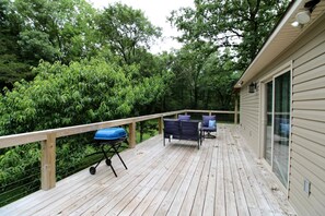 A wooden deck with a barbecue grill, outdoor furniture, and a view of dense greenery. - Charming Cottage Nestled Amidst Trees in Hot Springs, Arkansas (Hot Springs)