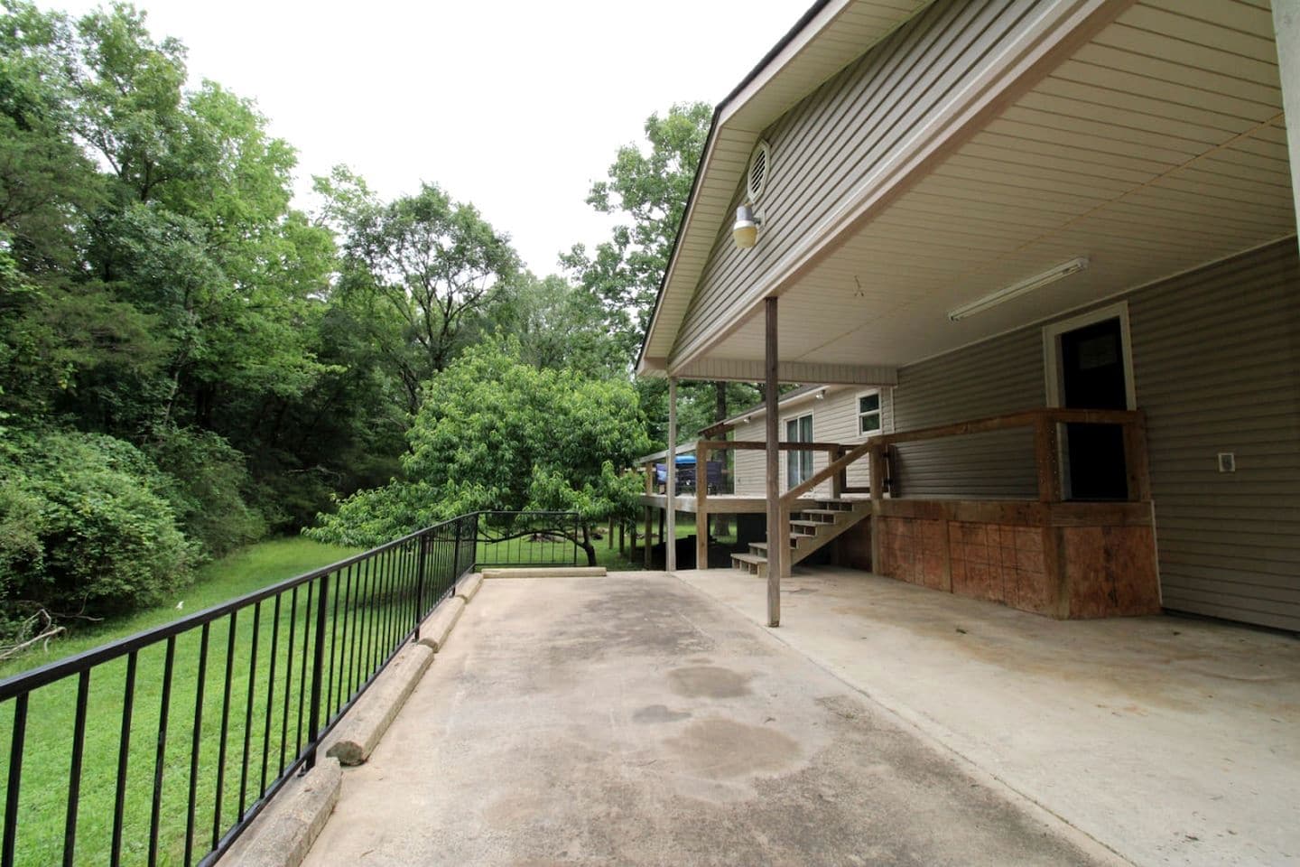 A covered outdoor area with a concrete floor, a wooden staircase, and a metal railing.