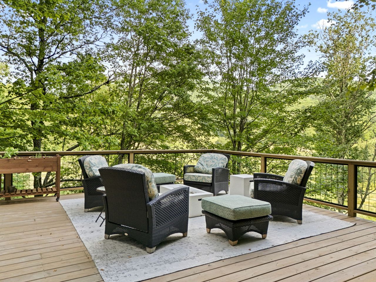 A deck with wicker furniture, a wooden table, and a white rug.